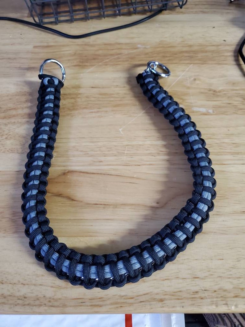 May include: A black and gray paracord leash with silver metal rings on each end.