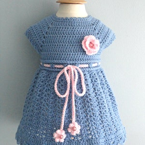 May include: A blue crocheted baby dress with pink flower embellishments and a pink ribbon tie.