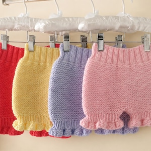 Peut inclure: Quatre paires de shorts en tricot suspendues à des cintres rembourrés blancs. Les shorts sont présentés en rouge, jaune, lavande et rose clair unis. Chaque paire possède une taille élastique côtelée et un ourlet à volants texturé.