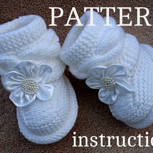 May include: A pair of white knitted baby booties with white satin flower embellishments. The booties are shown on a brown surface with the text "PATTERN instruction" below them.