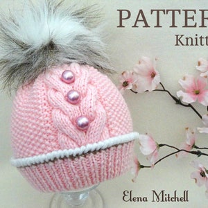 May include: Pink knitted hat with a white pom pom and pearl embellishments. The hat has a cable knit pattern and a white trim. The text "PATTERN Knitting" is visible in the image.