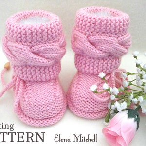 Può includere: Schema di lavoro a maglia per scarpine da neonato rosa con polsino intrecciato e un bottone in legno. Le scarpine sono su uno sfondo bianco con una rosa rosa e fiori bianchi.