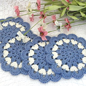 May include: Four crocheted blue and white coasters with a scalloped edge. The coasters are made with a delicate stitch pattern.
