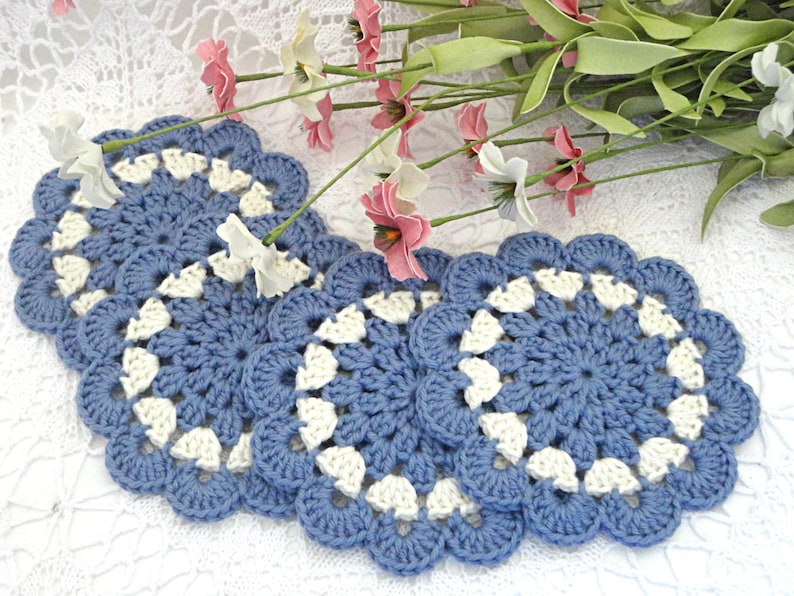 May include: Four crocheted blue and white coasters with a scalloped edge. The coasters are made with a delicate stitch pattern.