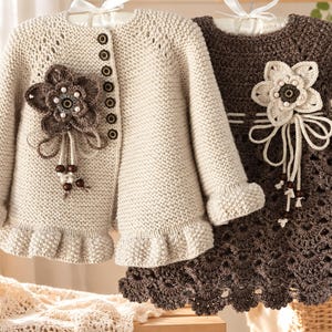 May include: A cream-coloured knit cardigan with a ruffled hem and a dark brown floral appliqué, paired with a dark brown crocheted dress featuring a cream-coloured floral appliqué and a scalloped hem, both displayed on hangers.
