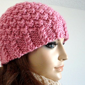 May include: A pink knitted hat with a textured pattern. The hat is made of soft yarn and has a comfortable fit.
