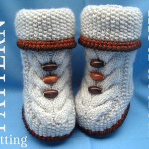 May include: A pair of knitted beige slippers with brown trim and wooden buttons. The slippers have a cable knit pattern.
