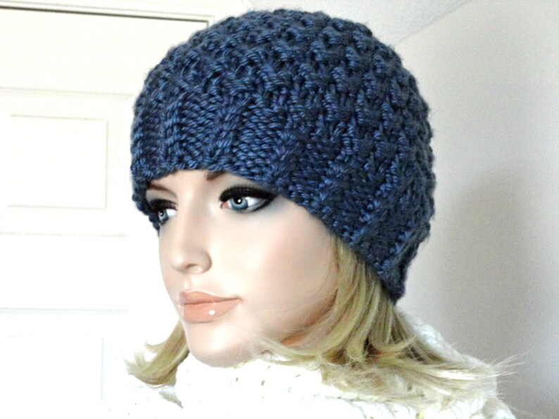 May include: A blue knitted beanie with a textured pattern. The beanie is worn by a person with blonde hair.