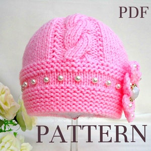 Puede incluir: Un gorro de beb&eacute; de punto rosa con un patr&oacute;n de trenza y un borde de perlas. El gorro tiene un adorno de flor con un centro de pedrer&iacute;a. El texto "PDF PATTERN" est&aacute; impreso debajo del gorro.