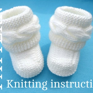 May include: A pair of white knitted baby booties with a cable knit pattern around the top. The booties are on a blue background.