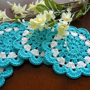 May include: Four crocheted turquoise and white coasters with a scalloped edge.