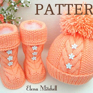 May include: A knitted baby hat and booties set in a peach color with white snowflake buttons. The hat has a pom pom on top. The pattern is a cable knit.