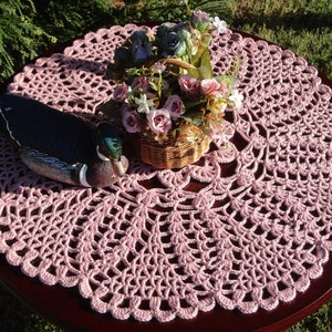 Peut inclure: Un chemin de table en crochet rose avec un motif d&eacute;coratif. Une figurine de canard en bois et un panier de fleurs sont pos&eacute;s sur le chemin de table.