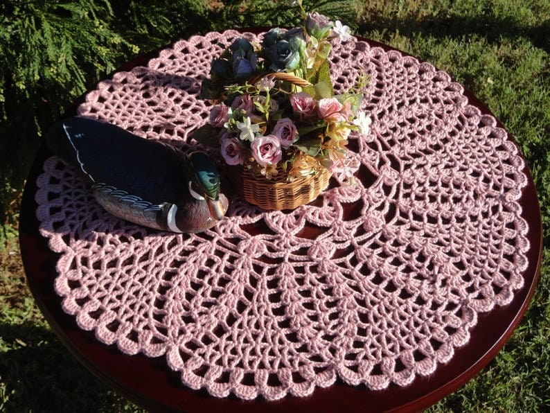 Peut inclure: Un chemin de table en crochet rose avec un motif d&eacute;coratif. Une figurine de canard en bois et un panier de fleurs sont pos&eacute;s sur le chemin de table.