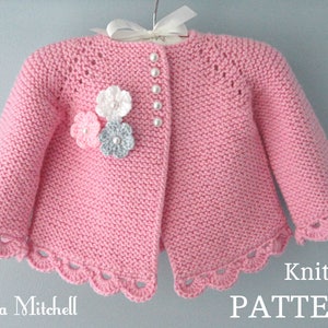 May include: Pink knitted baby cardigan with a crocheted flower embellishment and pearl buttons. Knitting pattern.