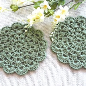 May include: Two green crocheted doilies with a scalloped edge. The doilies are made with a delicate stitch pattern and have a vintage look.
