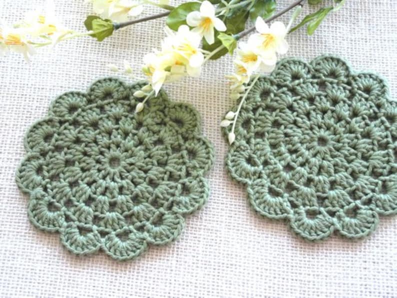 May include: Two green crocheted doilies with a scalloped edge. The doilies are made with a delicate stitch pattern and have a vintage look.