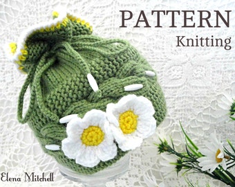 May include: Green knitted hat with white daisy flowers and a yellow center. The hat has a drawstring and is decorated with white beads. The hat is on a white lace background. PATTERN Knitting.
