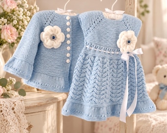 Puede incluir: Una chaqueta de punto azul claro y un vestido sin mangas a juego. La chaqueta presenta botones blancos y una flor de ganchillo blanca. El vestido tiene un patrón de trenzas, una cinta blanca en la cintura y una flor de ganchillo a juego.