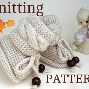 May include: Knitting pattern for a pair of beige baby booties with brown wooden beads. The booties have a cable knit design and are tied with yarn.
