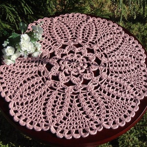 Peut inclure: Un chemin de table en crochet rose avec un motif floral d&eacute;licat. Le chemin de table est circulaire et a un bord festonn&eacute;.