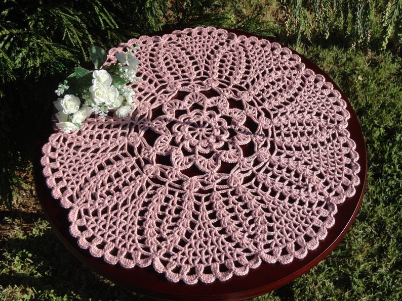 Peut inclure: Un chemin de table en crochet rose avec un motif floral d&eacute;licat. Le chemin de table est circulaire et a un bord festonn&eacute;.