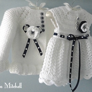 May include: White crocheted baby cardigan and dress set with black and white polka dot ribbon accents and black buttons.