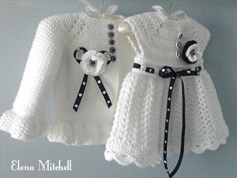 May include: White crocheted baby cardigan and dress set with black and white polka dot ribbon accents and black buttons.