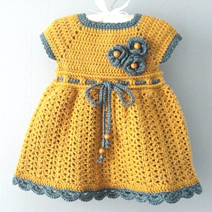 May include: A yellow crocheted dress with a gray crocheted trim and a gray crocheted flower detail. The dress has a tie at the waist.