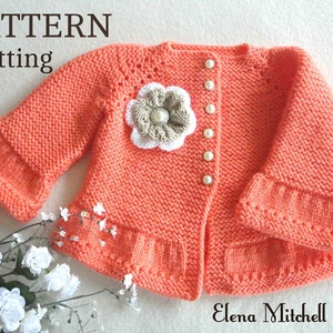 May include: A knitted baby cardigan in a peach colour with a white and beige flower embellishment and pearl buttons. The cardigan has a ruffled hem and bell sleeves. The text "PATTERN Knitting" is visible at the top of the image.