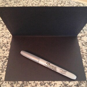 May include: A silver Sharpie permanent marker on a black card.
