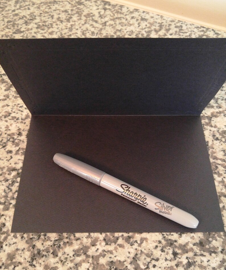 May include: A silver Sharpie permanent marker on a black card.