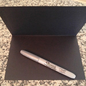 May include: A silver Sharpie permanent marker on a black card.