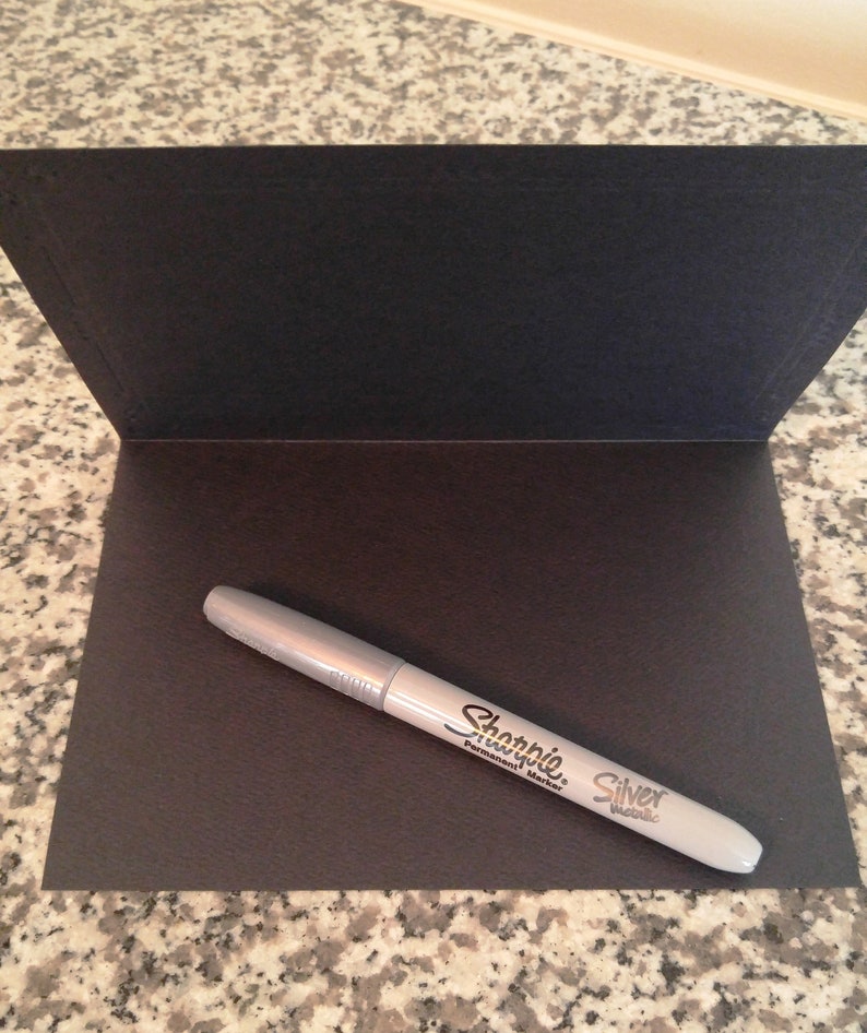 May include: A silver Sharpie permanent marker on a black card.