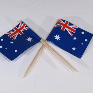 May include: Two small Australian flags on wooden skewers, crossed over each other. The flags are blue with a white star and a red Union Jack in the upper left corner.