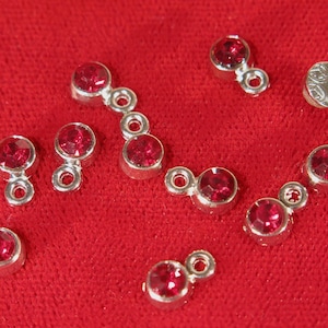 May include: A collection of silver-toned jewelry findings with small, red, round rhinestones. Each finding has a loop on one end and a small, round, red rhinestone on the other end.