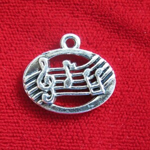 May include: Silver charm with a musical note design. The charm features a treble clef and musical notes on a staff.