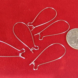 May include: Five silver teardrop-shaped earring hooks, displayed on a red surface, next to a US quarter for size comparison.