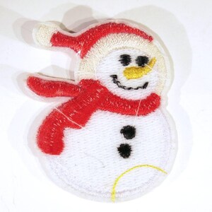 May include: White felt snowman applique with a red felt hat and scarf. The snowman has black eyes, a black button, and an orange felt nose.