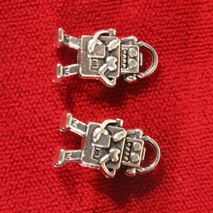 May include: Two silver robot charms with a heart design on the chest and a circular design on the face. The charms have a loop at the top for attaching to a bracelet or necklace.
