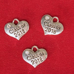May include: Three silver heart-shaped charms with a rhinestone on each. Each charm has the text "Class of 2018" engraved on it.