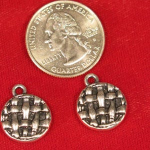 May include: Two silver-toned metal charms in the shape of a woven basket. The charms are about the size of a US quarter.