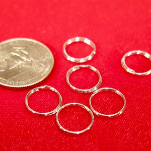May include: Six silver key rings on a red surface. The key rings are all the same size and are arranged in a circle.