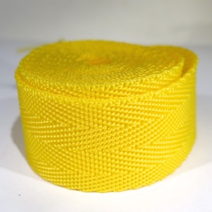 May include: A roll of bright yellow webbing with a diamond pattern. The webbing is tightly wound and has a smooth, even texture.