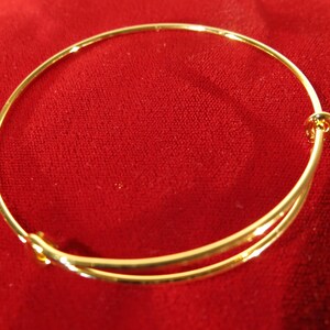 May include: A gold-toned adjustable bangle bracelet. The bracelet is made of thin metal and has a simple, elegant design.