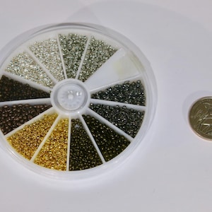 May include: A white plastic wheel with 12 compartments filled with different colored beads. The beads are small and round, and they are arranged in a circular pattern. The wheel is about the size of a US quarter.