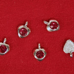 May include: Five silver charms with red gem accents. The charms are shaped like hearts and a spade.