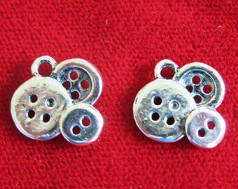 May include: Two silver charm pendants shaped like buttons. Each pendant features three buttons, one large and two smaller buttons.