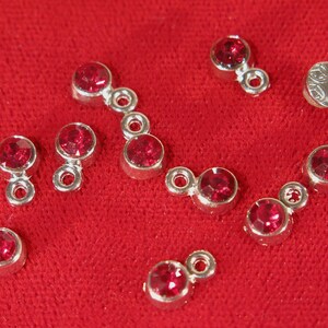 May include: A set of ten silver-toned jewelry connectors with red rhinestone accents. Each connector has two loops for attaching to other jewelry pieces.