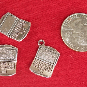 May include: Four silver charm pendants shaped like laptop computers. The charms are detailed with a textured surface and a keyboard design.